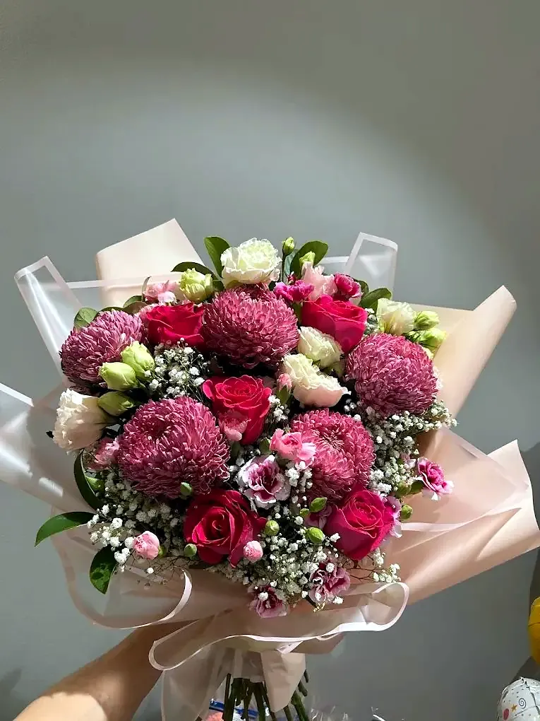 Burgundy chrysanthemums and red roses wrapped in pale pink paper