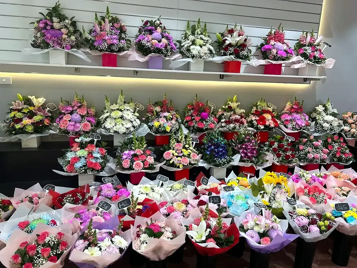 The bouquet wall inside Tran Florist: wrapped bouquets on a lit white shelf, with rows more in buckets below